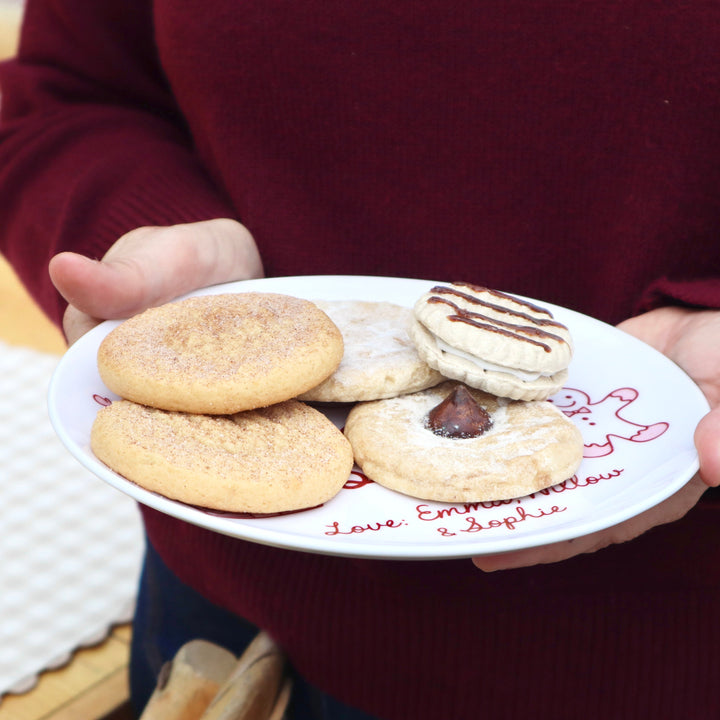 Plate filled with cookies held by hands.