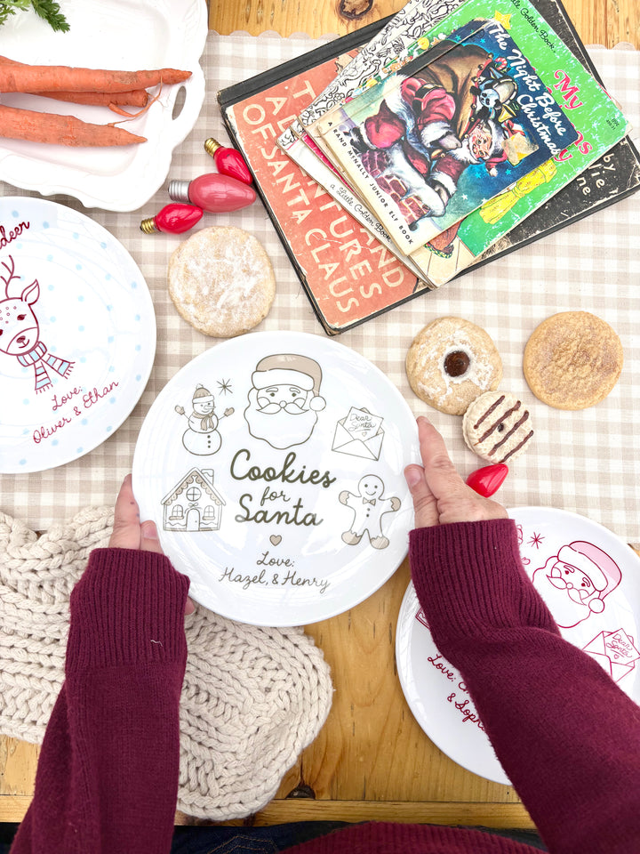 Christmas plates, cokies, books on table. Christmas Eve inspired setting. Hands holding ceramic santa plate